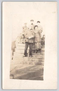 Postkarte RPPC Familiengruppe zusammengekauert auf Außentreppen - Winterjacken und Mützen - Bild 1 von 4