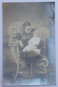 Niña joven sentada en silla ornamentada sosteniendo muñeca grande postal RPPC AZO 3172 - Imagen 1 de 3