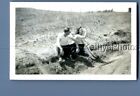 FOUND B&W PHOTO C+9999 MAN SITTING ON SIDE OF ROAD WITH PRETTY WOMAN HOLDING NOS