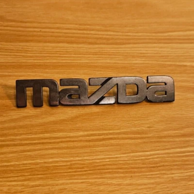 86-89 Mazda 323 "Mazda" Plastic Trunk Emblem - P/N - BF6751780781-1 - As Removed - Image 1 of 4