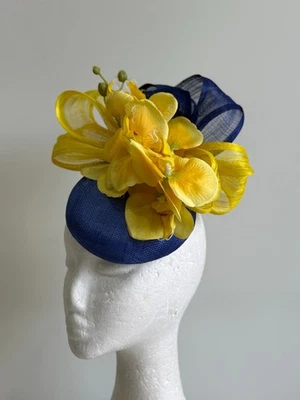 Fascinador base azul con lazos azules y amarillos y flores de orquídea amarillas. Foto 1 de 4