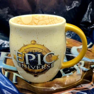 EPIC Universe Universal Studios Logo Emblem Elfenbein Kaffeebecher Tasse Gold Henkel NEU - Bild 1 von 3