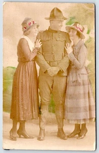RPPC WWI era SOLDIER SMILES at 2 WOMEN HAND-COLORED ANTIQUE REAL PHOTO POSTCARD - Picture 1 of 2