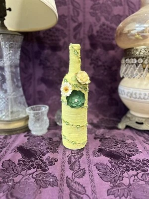 Botella de vino decorativa envuelta en cadena amarilla acentuada con flores verdes Foto 1 de 3