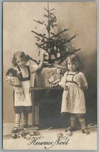 SCHWESTERN mit PUPPEN UNTER GESCHMÜCKTEM WEIHNACHTSBAUM ANTIK ECHTFOTO POSTKARTE RPPC - Bild 1 von 2