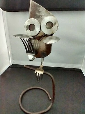 Búho esculpido sentado en soporte hecho de cucharas, tenedores, arandelas y metal Foto 1 de 4