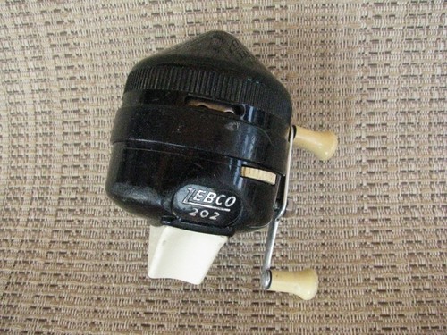 Black Zebco 202 spin casting reel with silver handle, made in USA, on woven surface with diagonal stripes.