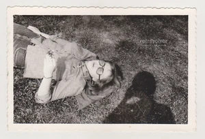 Young Woman Lying on Grass with a Flower Photographer's Shadow Cast Beside Her - Picture 1 of 7