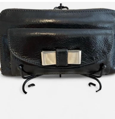 Cartera continental Chloe de cuero negro con cremallera alrededor con acento de lazo dorado Foto 1 de 4