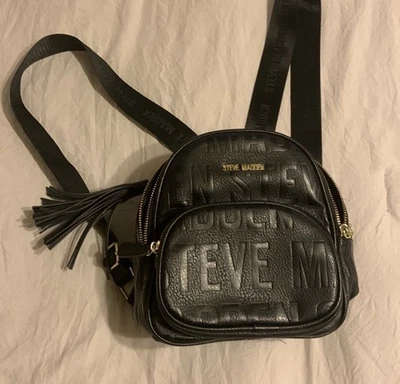 Mini Mochila Steve Madden Logo Negra Con Nombre Cremalleras y Borla Dije Foto 1 de 2