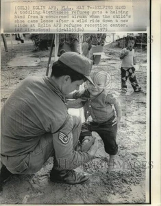 1975 Press Photo Vietnamese Toddler Refugee Gets Help with Shoe from Airman - Picture 1 of 2
