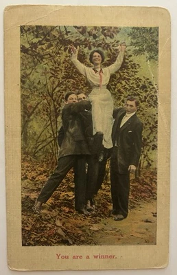 Postal de colección "Eres un ganador" hombres sosteniendo a mujer divertido camino forestal Foto 1 de 2