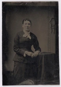 Vestido oscuro de dama de pie, corpiño ajustado, pendientes, foto tipo retrato de estudio - Imagen 1 de 2