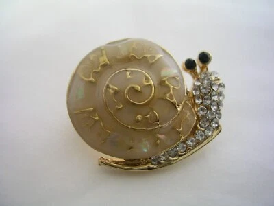 БУЛАВКА УЛИТКА С БЕЖЕВОЙ ЭМАЛЬЮ, ЧЕРНЫЙ ОНИКС И КРИСТАЛЛЫ В ЗОЛОТОЙ ТОНИРОВАННОЙ НЕРЖАВЕЮЩЕЙ СТАЛИ - Изображение 1 из 4