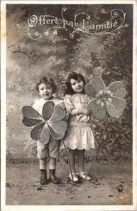 TWO ADORABLE CHILDREN HOLDING LARGE FLOWERS : OFFERED IN FRIENDSHIP : RPPC - Picture 1 of 3