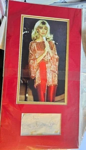Firma OLIVIA NEWTON-JOHN in ESPOSITORE FOTOGRAFICO OPACO... con grasso COA 19x10 - Foto 1 di 5