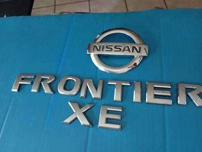 NISSAN FRONTIER XE LETRAS CROMADAS 2005-16 ESCOTILLA TRASERA EMBLEMAS LOGOTIPO USADO OEM  Foto 1 de 4