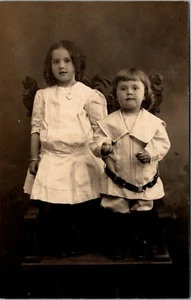 Adorable hermano y hermana de pie en silla RPPC - Imagen 1 de 2