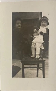 Postal con foto real RPPC ~ Dos niñas sentadas en silla brazos con muñeca - Imagen 1 de 2