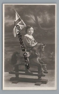 RPPC Patriotisches Mädchen auf Spielzeug SCHAUKELPFERD und Union Jack Flagge Echtfoto Postkarte - Bild 1 von 2