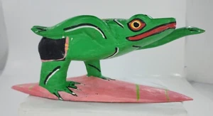 Handgeschnitzter Frosch aus Holz auf rosa Surfbrett mit grünen Streifen handbemalt - Bild 1 von 7