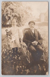 RPPC Cute Adorable Girl Holding Antique Doll Posing with Older Cigar Smoking Man - Picture 1 of 6