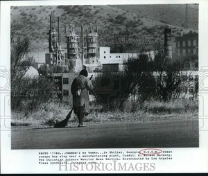 Pressefoto Frau fegt Bushaltestelle nahe Produktionsstätte in Georgia, UdSSR - Bild 1 von 2