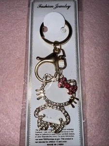 HELLO KITTY Schlüsselanhänger/Taschenanhänger Strass Umriss goldfarben mit dunkelrosa Schleife - Bild 1 von 4