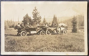 Cartolina fotografica reale RPPC molte persone e due automobili in campo vicino alle montagne - Foto 1 di 3