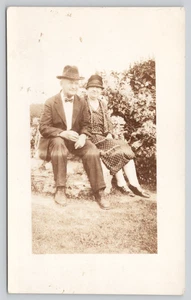 Postkarte RPPC älterer Mann und Frau sitzen auf Felsen - Fliege Fedora gepunktetes Kleid - Bild 1 von 4