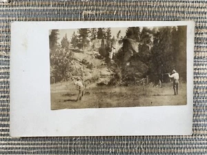 RPPC Mann Luftgewehr auf einen anderen Mann Arme erhöhte Entfernung Echtfoto Postkarte - Bild 1 von 2