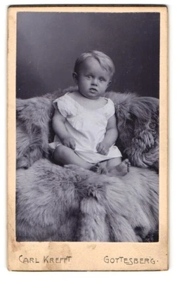 Fotografie Carl Krefft, Gottesberg, Blondes Kind im weißen Gewand auf einem Pel  - Bild 1 von 2