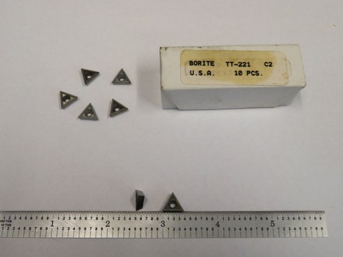 Seven metal TT-221 C2 carbide inserts with triangular black tips, shown beside labeled brown cardboard box.