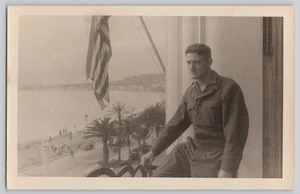 Foto real de soldado de la Segunda Guerra Mundial con bandera de Estados Unidos palmeras escena costera RPPC - Imagen 1 de 3