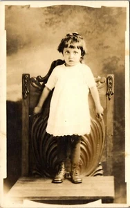 Foto postal vintage RPPC niña asustada de pie en silla antigua estudio - Imagen 1 de 3