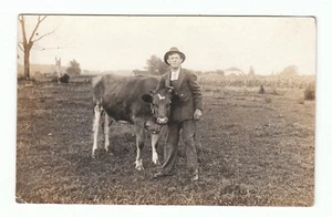 Vintage RPPC Echt Foto Postkarte Mann im Anzug Hut mit seiner Kuh auf einem Feld Sammlerstück - Bild 1 von 2