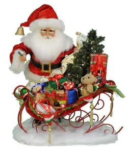 WEIHNACHTSMANN FIGUR MIT SPIELZEUG GEFÜLLTEM SCHLITTEN UND BELEUCHTETEM WEIHNACHTSBAUM - Bild 1 von 1