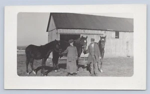 Hombre y mujer posando con caballos y granero fotografía real postal RPPC - Imagen 1 de 2