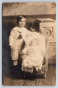 Postkarte Unbekannt RPPC Baby Mädchen Korbstuhl neben Kleinkind Bruder c1909 - Bild 1 von 2
