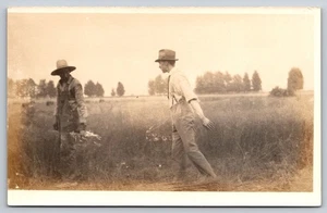 Two Young Men One in Suspenders & Fedora Walking Through Tall Grassy Field RPPC - Picture 1 of 2