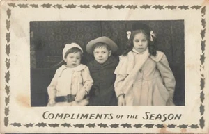 Postcard RPPC Christmas Compliments of the Season Three Children. Australian? - Bild 1 von 2