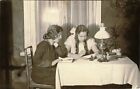 TWO GIRLS SIT AT THE TABLE IN LEAVING ROOM & VINTAGE OCCUPATIONAL PHOTO POSTCARD