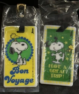 2 VINTAGE SNOOPY PLASTIC LUGGAGE TRAVEL TAGS NEW HAVE A GREAT TRIP BON VOYAGE - Picture 1 of 4