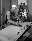 Man wearing bib overalls & a cap applying wallpaper paste a brush  Old Photo