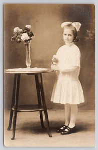 RPPC Young Girl White Bow Posing Next to Table Flowers Identified CYKO Postcard - Picture 1 of 2